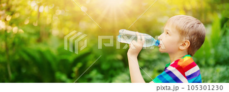 Boy standing in the natural park and drinking water from transparent bottle. Boy standing in the natural park and drinking water from transparent bottle. 105301230