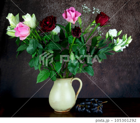 Flowers in an Earthenware Wine Jug with Bunch of Grapes on a Wooden Table Top Flowers in an Earthenware Wine Jug with Bunch of Grapes on a Wooden Table Top 105301292