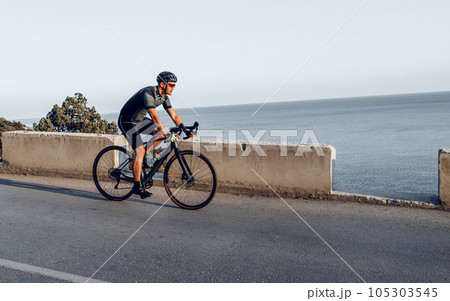 Man cyclist pedaling on a road bike outdoors in sun set 105303545