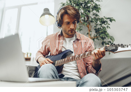 Man playing electric guitar and recording music into laptop 105303747