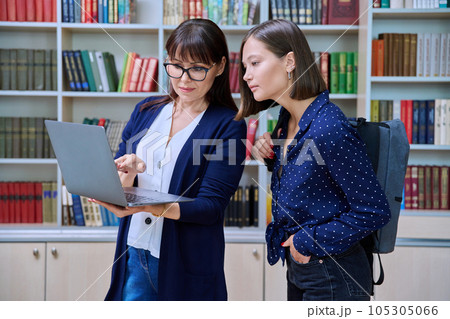 Female teacher with young college student talking while looking at laptop together, in library Female teacher with young college student talking while looking at laptop together, in library 105305066