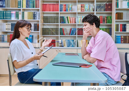 Female college counselor talking with young male student, meeting in library 105305087
