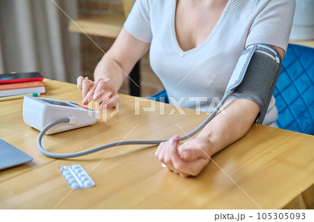 Middle-aged woman sitting at home, measuring blood pressure with tonometer 105305093