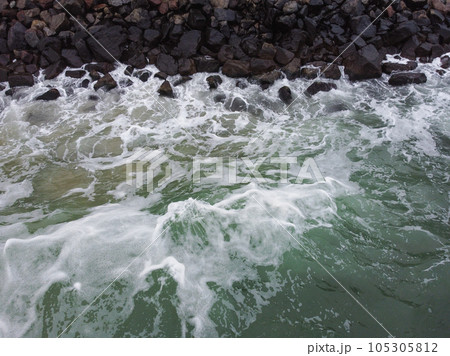 Aerial view of the ocean waves in the sea banging on the rocks. 105305812