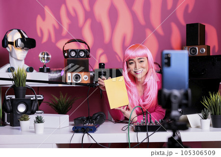 Smiling asian content creator holding notebook presenting school product in front of phone camera while filming review in broadcast studio. Influencer live streaming using vlogging equipment 105306509