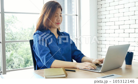 Asian Female freelance using laptop at home office desk. Woman reading financial graph chart Planning analyzing marketing data. Asian female people working office firm with business stuff, coffee cup 105312146