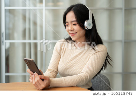 A happy Asian woman is using her smartphone while listening to music on her headphones 105318745
