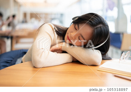 A beautiful Asian woman is listening to music on her headphones and falling asleep on a table 105318897