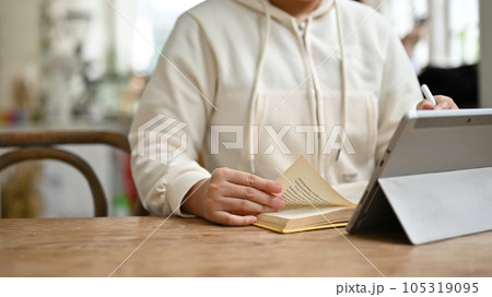 Cropped image of a woman reading a book and working on her project on her digital tablet Cropped image of a woman reading a book and working on her project on her digital tablet 105319095