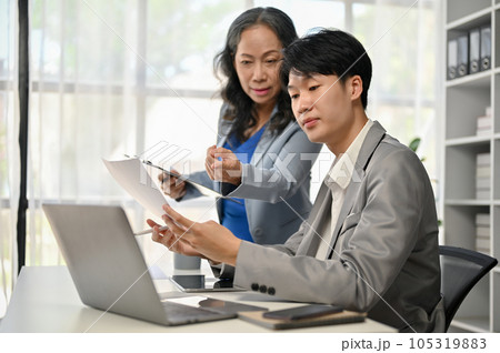 A senior female boss is co-working on a new project with a young male worker 105319883
