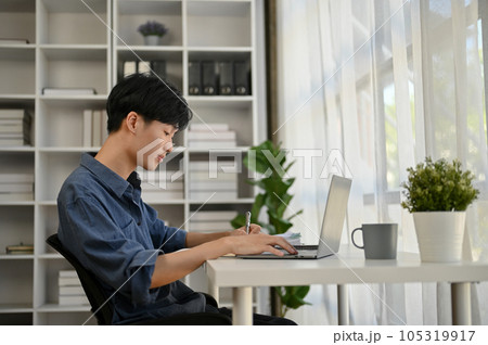 A serious and focused young Asian male office worker is working on his work on his laptop A serious and focused young Asian male office worker is working on his work on his laptop 105319917