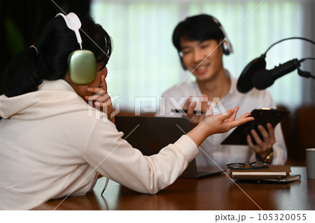 Back view of female broadcaster wearing headphone interviewing her guest at small home studio 105320055