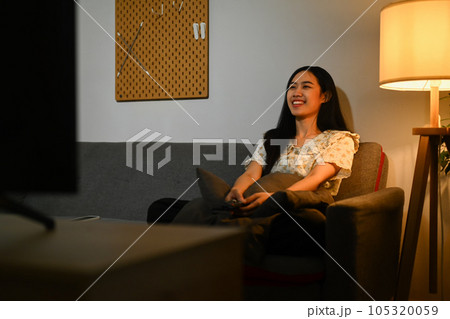 Joyful young woman watching romantic movie on TV at home in evening alone Joyful young woman watching romantic movie on TV at home in evening alone 105320059