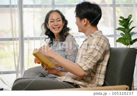 A happy Asian grandmother is laughing while talking and reading a book with her grandson A happy Asian grandmother is laughing while talking and reading a book with her grandson 105320237
