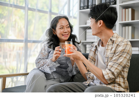 A cute Asian grandson is giving a glass of orange juice to his grandmother 105320241