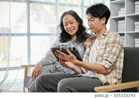 A happy Asian grandson enjoys watching funny videos on his tablet with his grandmother 105320243