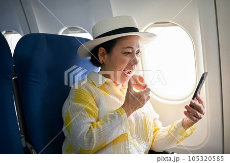 A happy female passenger enjoys eating doughnuts and using her smartphone during the flight A happy female passenger enjoys eating doughnuts and using her smartphone during the flight 105320585
