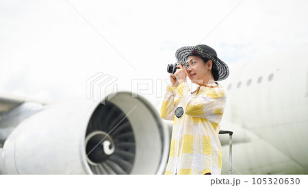 A portrait of a happy senior Asian female tourist taking pictures with her film camera at the airport. 105320630