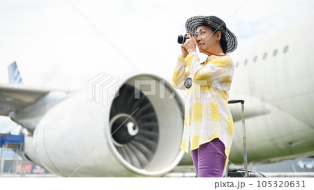 A happy senior Asian female tourist taking pictures with her film camera at the airport. 105320631
