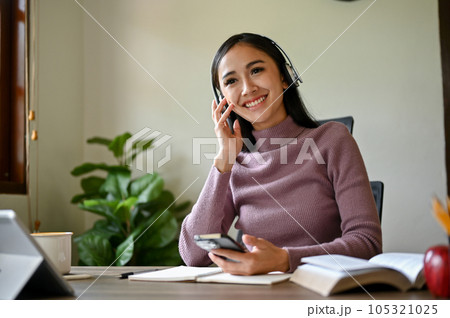 A happy Asian woman enjoys listening to music through her wireless headphones at her desk. A happy Asian woman enjoys listening to music through her wireless headphones at her desk. 105321025