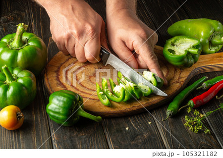 The chef cuts green pepper on a cutting board for making spicy adjika. Peasant delicious food 105321182