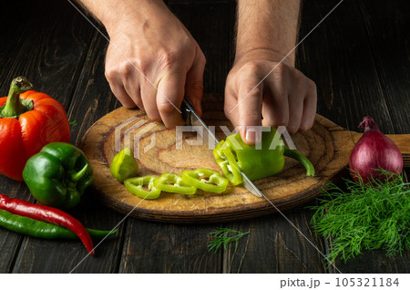 Close-up of the cook hands with a knife cut fresh pepper on the cutting board of the restaurant kitchen. Vegetarian diet Close-up of the cook hands with a knife cut fresh pepper on the cutting board of the restaurant kitchen. Vegetarian diet 105321184
