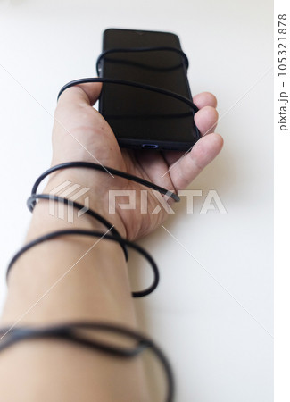 Overcoming phone addiction. Man hand is wrapped around the wire of smartphone charger. Conceptual photo of smartphone addiction. Loss of ability to live normal life. Negative impact of digitalization 105321878