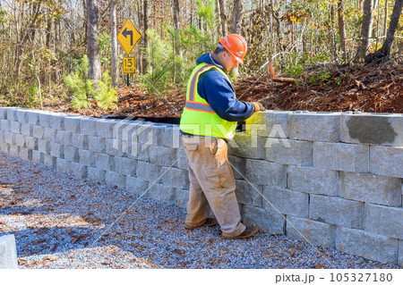 During development of new property, construction worker is using cement blocks for building retaining wall. During development of new property, construction worker is using cement blocks for building retaining wall. 105327180