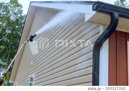 Water soap cleaner is sprayed onto siding houses by service worker, employing high pressure nozzles. 105327202