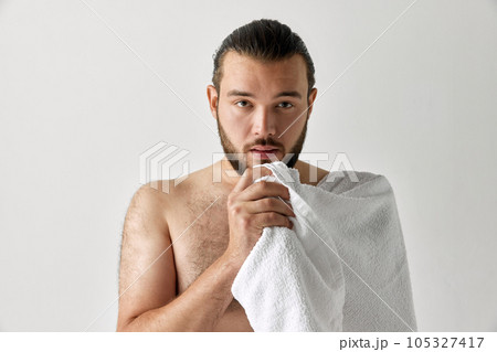 Portrait of serious man with towel on his shoulder looking at camera. Male facial care. Bearded man. 105327417