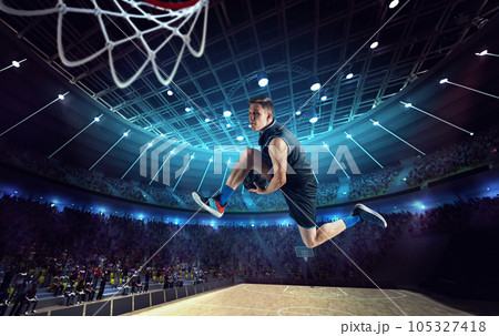 Slam dunk. Young man, professional basketball player on 3D stadium, arena during game, jumping with ball Slam dunk. Young man, professional basketball player on 3D stadium, arena during game, jumping with ball 105327418