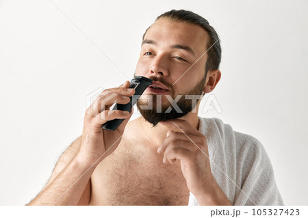 Closeup portrait of virile man shaving mustache isolated over light grey background. Bearded man. 105327423
