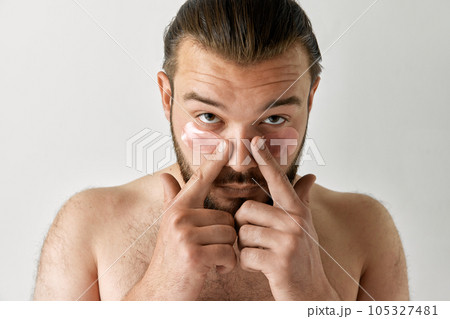 Focused man lowered his head and smoothed patches under his eyes over isolated grey background. Focused man lowered his head and smoothed patches under his eyes over isolated grey background. 105327481