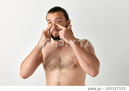 Portrait of handsome man having beard looking away and toching area under eyes over grey background. 105327535