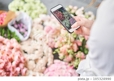 A woman takes a photo on her phone of flowers. Floral shop concept . Florist woman creates flower arrangement in a wicker basket. . Flowers delivery. A woman writes a video blog or online course A woman takes a photo on her phone of flowers. Floral shop concept . Florist woman creates flower arrangement in a wicker basket. . Flowers delivery. A woman writes a video blog or online course 105328990