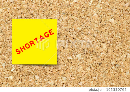 Yellow note paper with word shortage on cork board background with copy space 105330765