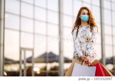 Woman in shopping. Young girl in protective sterile medical mask on her face with shopping bags. Woman in shopping. Young girl in protective sterile medical mask on her face with shopping bags. 105332097