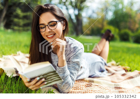 Beautiful relaxed woman readingbook at lawn with sun shining. Girl gets pleasure from reading book. Beautiful relaxed woman readingbook at lawn with sun shining. Girl gets pleasure from reading book. 105332342
