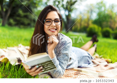 Beautiful relaxed woman readingbook at lawn with sun shining. Girl gets pleasure from reading book. Beautiful relaxed woman readingbook at lawn with sun shining. Girl gets pleasure from reading book. 105332343