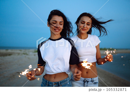 Three beautiful girls celebrating, holding sparklers on the beach at night. . Summer holidays, vacation. Three beautiful girls celebrating, holding sparklers on the beach at night. . Summer holidays, vacation. 105332871