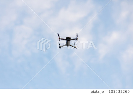 Drone flying on blue sky with white clouds background. Bottom view Quadcopter with digital camera. Flying remote control Quadrocopter, UAV. Drone flying on blue sky with white clouds background. Bottom view Quadcopter with digital camera. Flying remote control Quadrocopter, UAV. 105333269