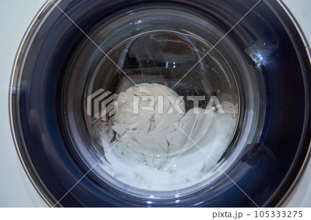 Wet white laundry in the drum of the washing machine. Close-up glass door from the washing machine with space for copying. High quality photo 105333275