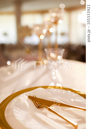 table decoration with pink tablecloth, crystal candlesticks with candles and white pink flowers in restaurant . stylish wedding day. setting table with gold plate, fork and knife table decoration with pink tablecloth, crystal candlesticks with candles and white pink flowers in restaurant . stylish wedding day. setting table with gold plate, fork and knife 105333921