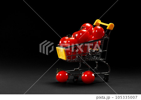 Mini shopping cart with cherry tomatoes on black background. Healthy eating and vegetarian food, cooking concept. selective focus. copy space. 105335007