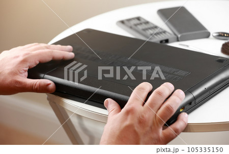 Repairman's hands removing the power battery from the laptop. Computer service and repair concept. Laptop disassembling in repair shop. Electronic development, electronic device fixing. Repairman's hands removing the power battery from the laptop. Computer service and repair concept. Laptop disassembling in repair shop. Electronic development, electronic device fixing. 105335150