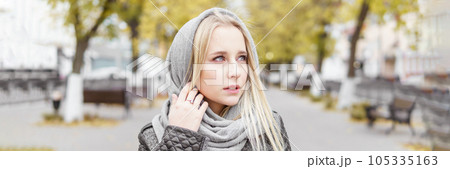 A young blonde walks through the autumn city in a gray coat. The concept of urban style and lifestyle. A young blonde walks through the autumn city in a gray coat. The concept of urban style and lifestyle. 105335163