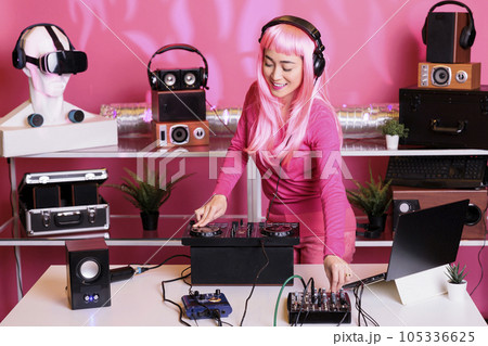 Musical artist with pink hair playing techno song at professional mixer console, enjoying performing music in club during night time. Asian performer mixing sounds in studio with isolated background Musical artist with pink hair playing techno song at professional mixer console, enjoying performing music in club during night time. Asian performer mixing sounds in studio with isolated background 105336625