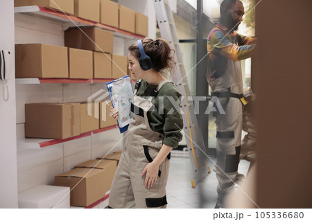 Warehouse employee working at products delivery, looking at shelves full with cardboard boxes. Storage room supervisor listening music while checking customers shipping details in storehouse 105336680