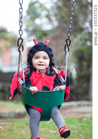 Little baby girl wearing a ladybug costume sitting on a toddler Swing. Halloween concept. Little baby girl wearing a ladybug costume sitting on a toddler Swing. Halloween concept. 105337325