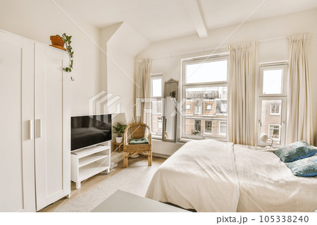 a bedroom with a bed, dresser and television in the corner of the room on the left is a large window a bedroom with a bed, dresser and television in the corner of the room on the left is a large window 105338240